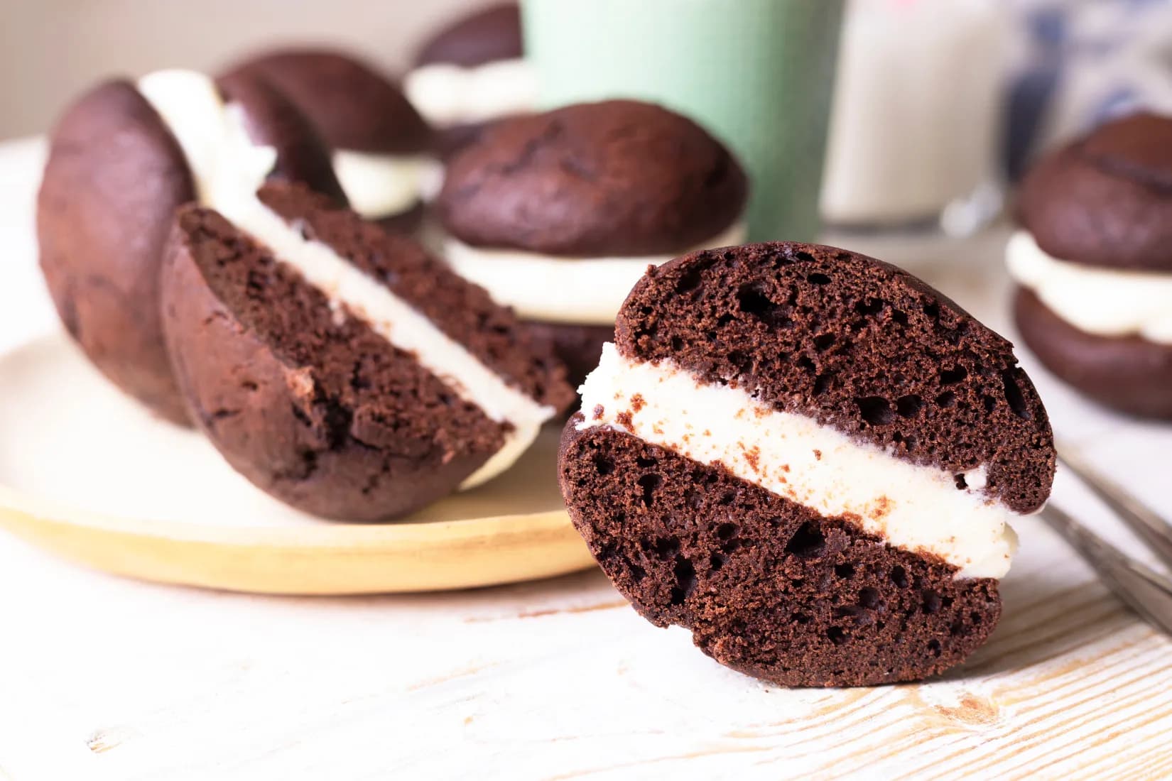 Chocolate whoopie pies with a thick layer of vanilla cream filling, displayed on a plate with one cut open to show the inside.